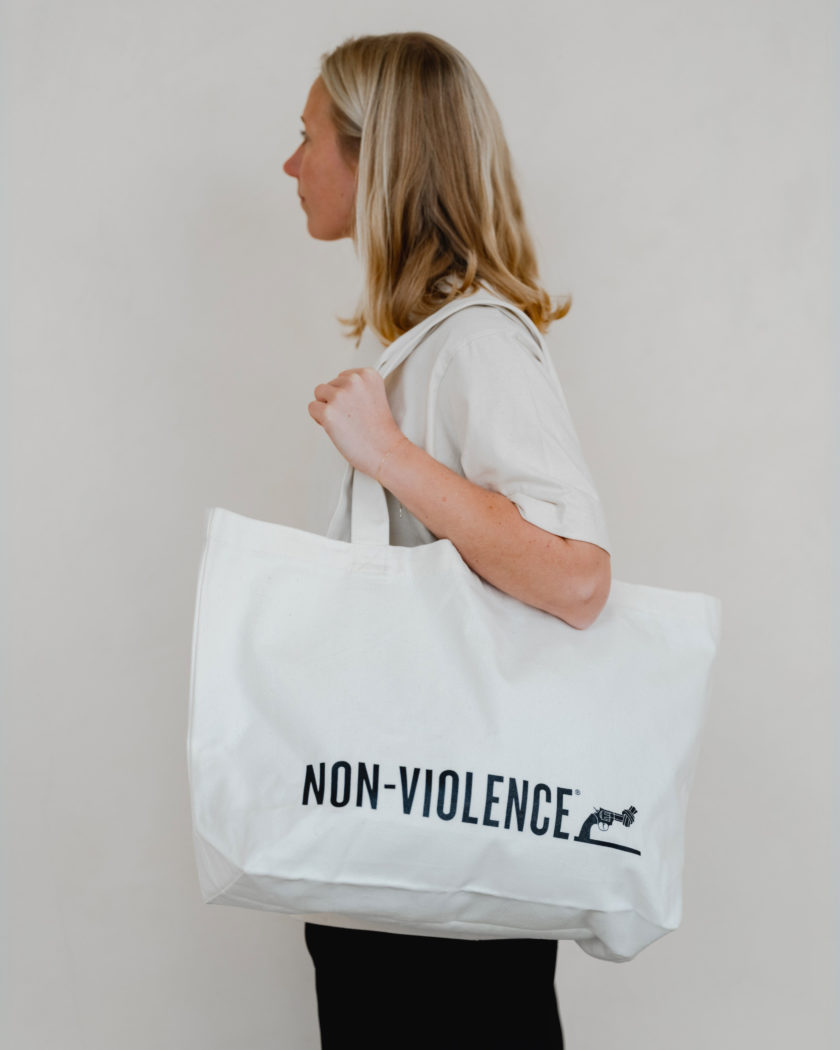 A woman with a Non-Violence Tote bag designed with a Non-Violence logo on the front.